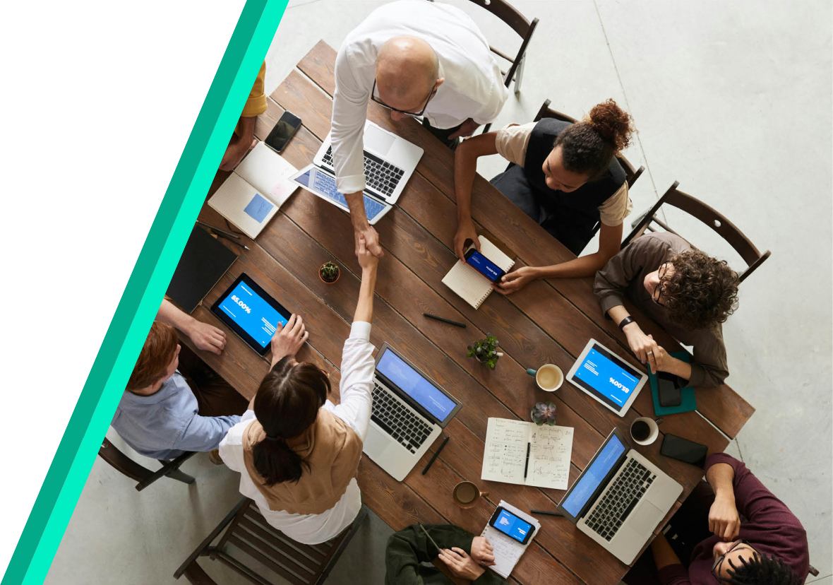 overhead photo of team of people sitting at a table together with their laptops and tablets